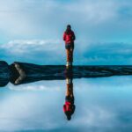 A solitary person is standing on a highly reflective surface creating a mirror effect