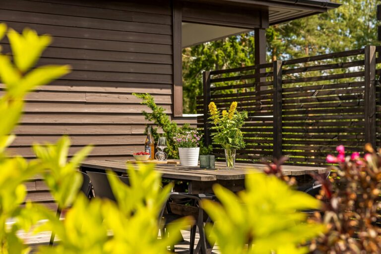 Outdoor patio with wooden table, chairs, and vibrant plants in summer.